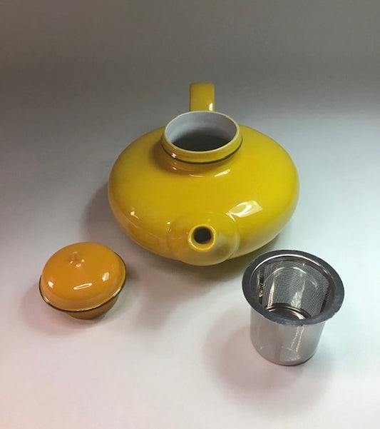 Yellow ceramic teapot with a metal tea infuser on a light gray background