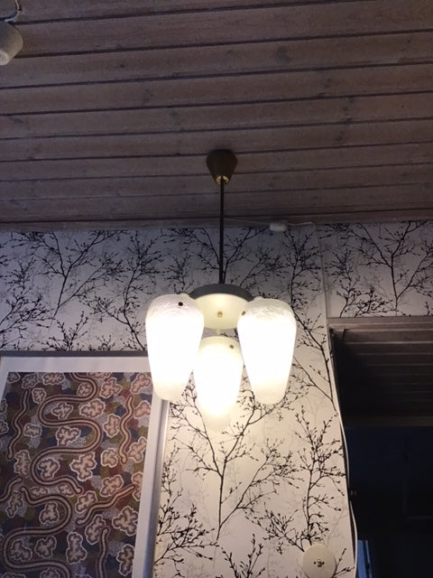 Floor lamp with multiple white lampshades in a room with patterned wallpaper and wooden floor.