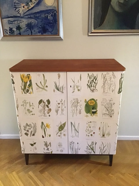 Cabinet with botanical pattern on a wall next to framed pictures