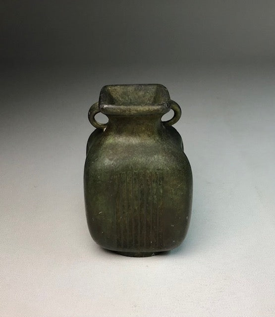 Small greenish-brown ceramic jar with two handles on a gray background