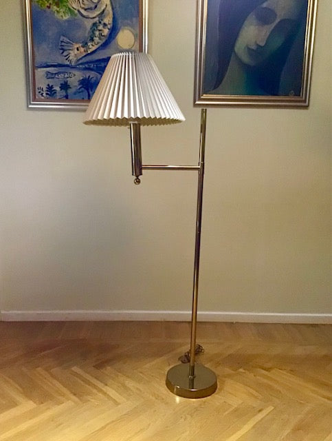 Floor lamp with pleated shade on a wooden floor, framed artwork in the background