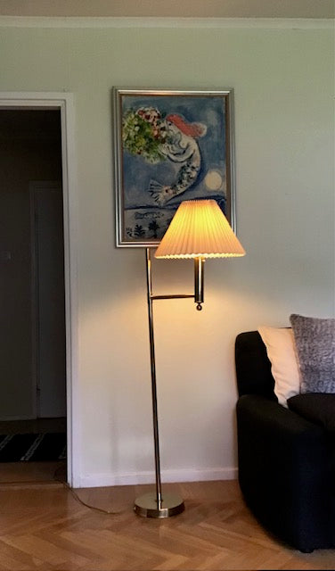 Floor lamp with a light on in a room with a painting and sofa.