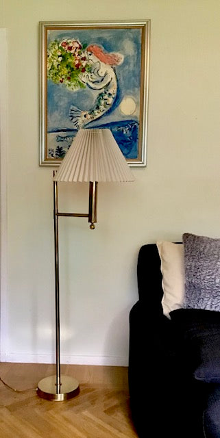 Floor lamp with pleated white shade next to a sofa and a painting on the wall.