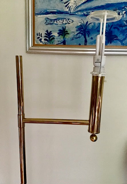 Copper floor lamp with a white shade against a wall with a decorative painting.