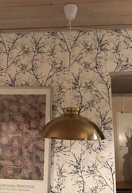 Gold pendant light fixture hanging in a room with patterned wallpaper and framed artwork.