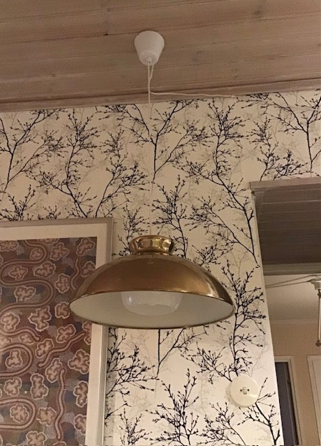 Gold pendant light hanging from a wooden ceiling with floral wallpaper in the background