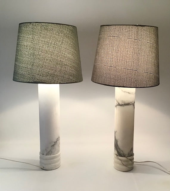 Two table lamps with marble bases and fabric shades on a neutral background