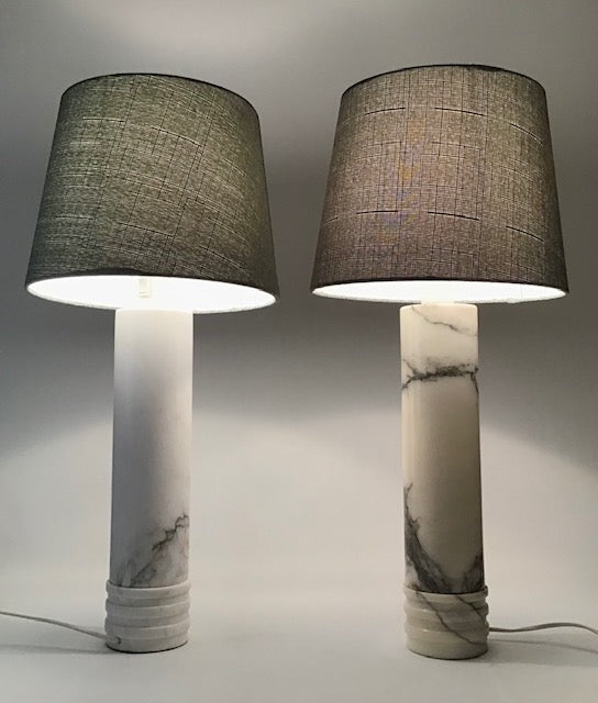 Two table lamps with marble bases and dark gray lampshades on a neutral background