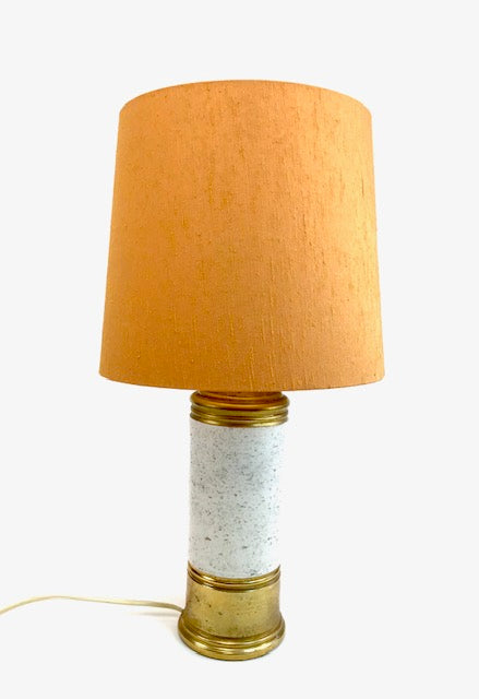 Table lamp with a mustard yellow shade and white and gold base on a light gray background