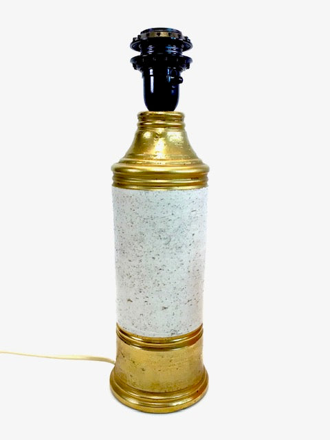 Decorative lamp with gold base and white speckled shade on a white background