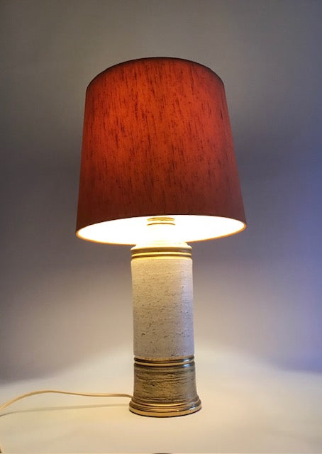 Table lamp with a red shade and beige base on a neutral background