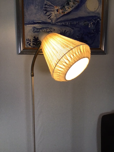 Floor lamp with a woven shade on a gray floor next to a framed picture