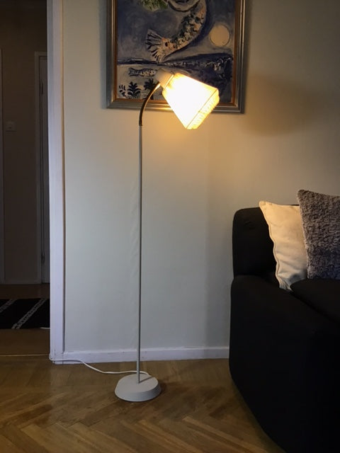Floor lamp on a wooden floor next to a white cabinet with a painting on the wall.