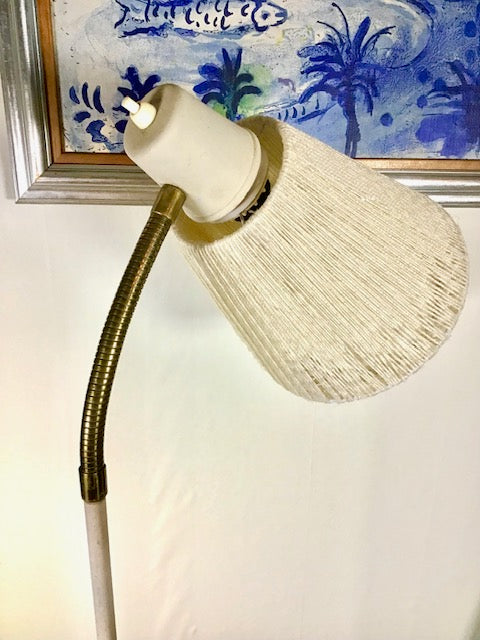 Beige lamp with flexible neck against a white wall with a framed artwork in the background