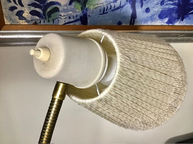 Light fixture with textured shade and brass arm against a decorative wall