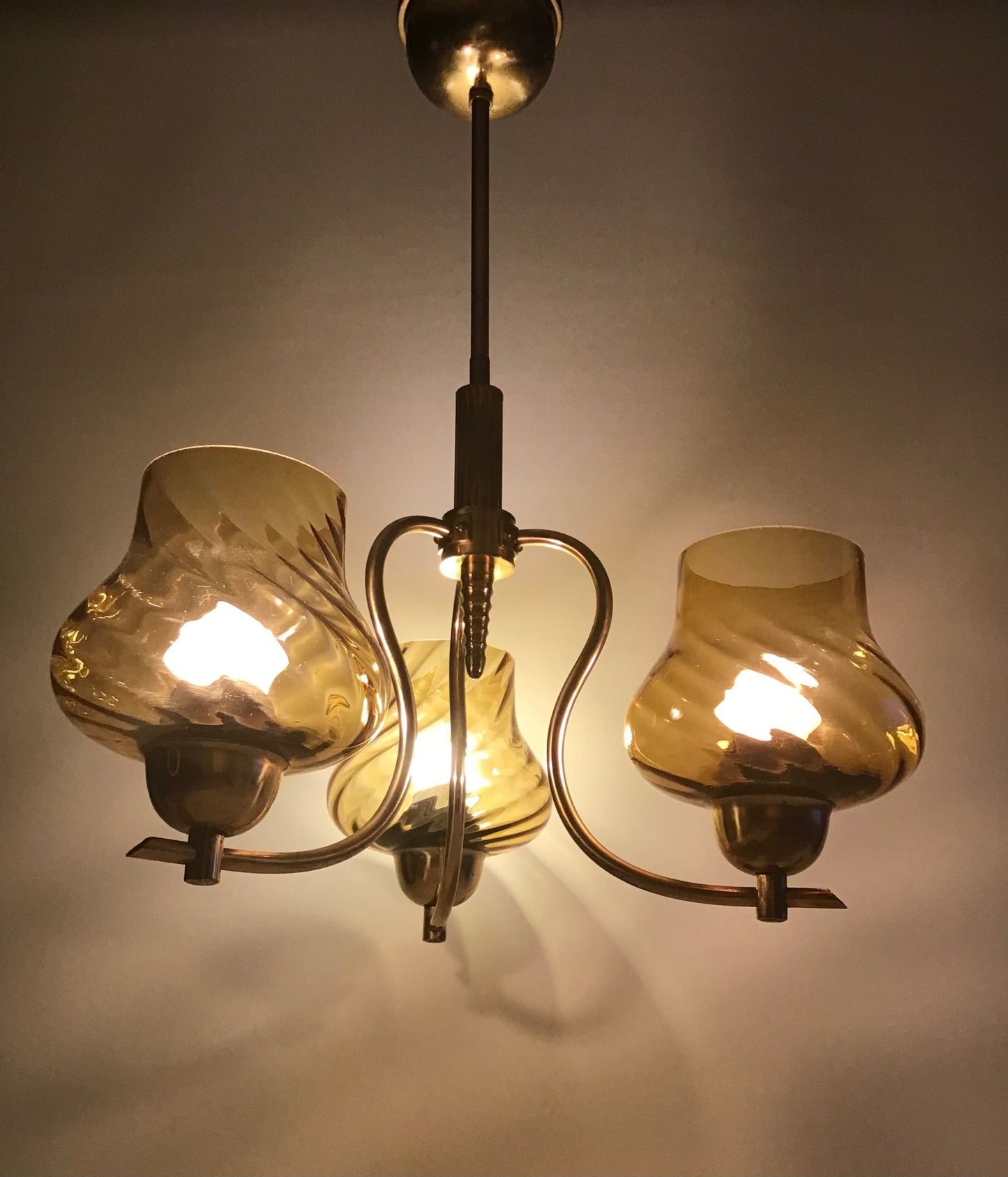 Vintage-style chandelier with three amber glass shades on a plain background