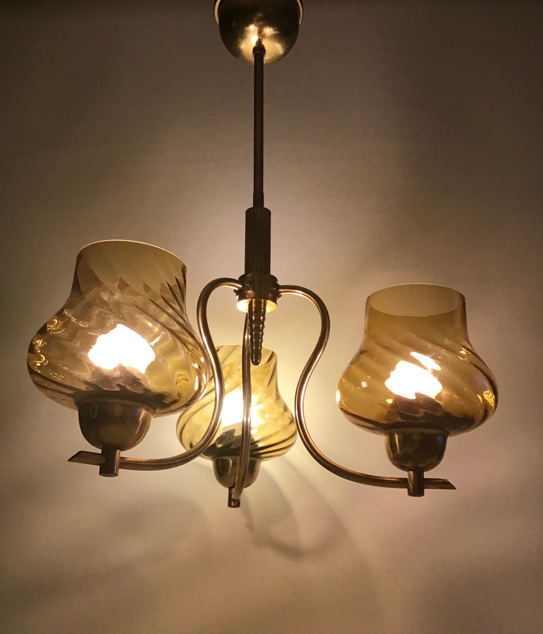 Vintage-style chandelier with three amber glass shades on a plain background