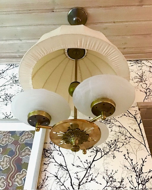 Vintage-style chandelier with white glass shades and brass fixtures against a neutral background.
