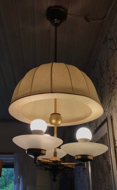 Chandelier with beige lampshade and glass shades in a dimly lit room.