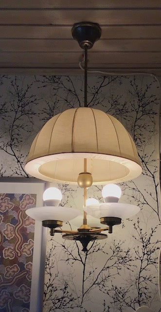 Chandelier with beige shade and gold accents against a decorative wall.