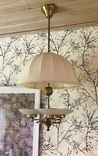 Vintage-style chandelier with beige lampshade against a decorative wall.