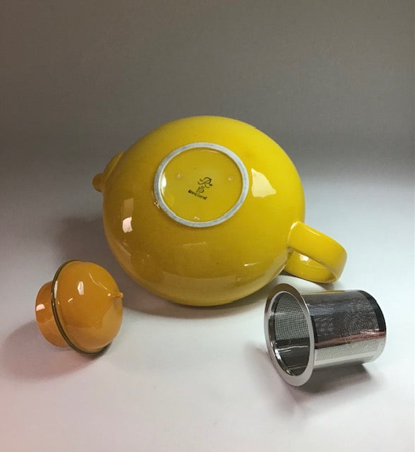 Yellow ceramic teapot with a lid and metal filter on a gray background