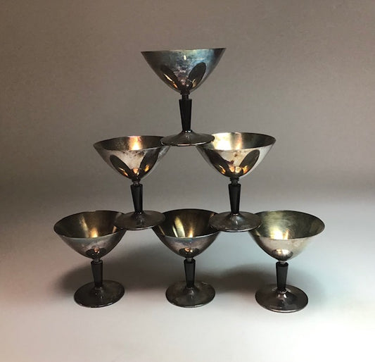 Set of six silver cocktail glasses arranged in a pyramid formation on a neutral background