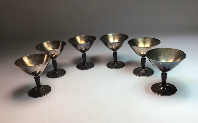 Set of eight metallic cocktail glasses on a white surface with a gray background