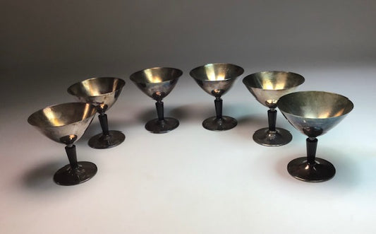 Set of eight metallic cocktail glasses on a white surface with a gray background
