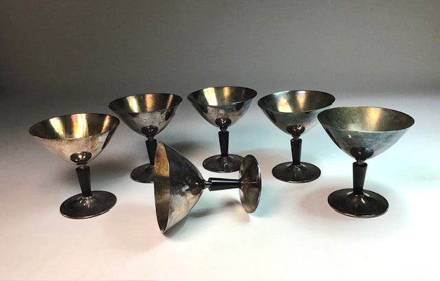 Set of six metallic cocktail glasses on a reflective surface with a gray background