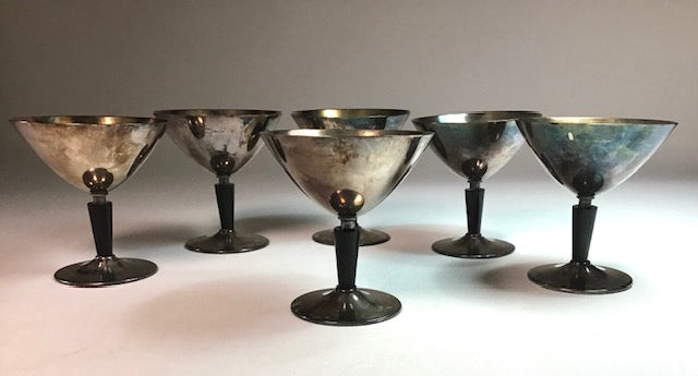 Set of six metallic cocktail glasses with black stems on a light background