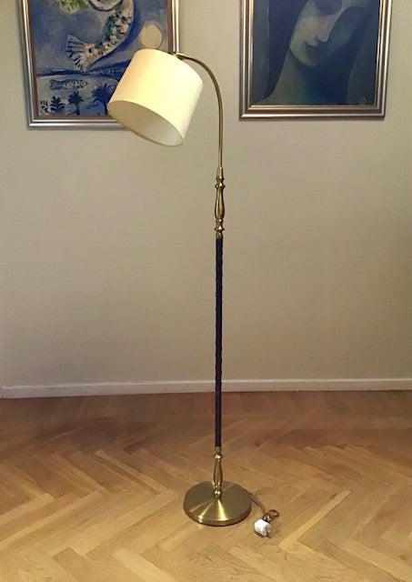 Floor lamp with a white shade on a wooden floor, with two framed artworks on the wall.