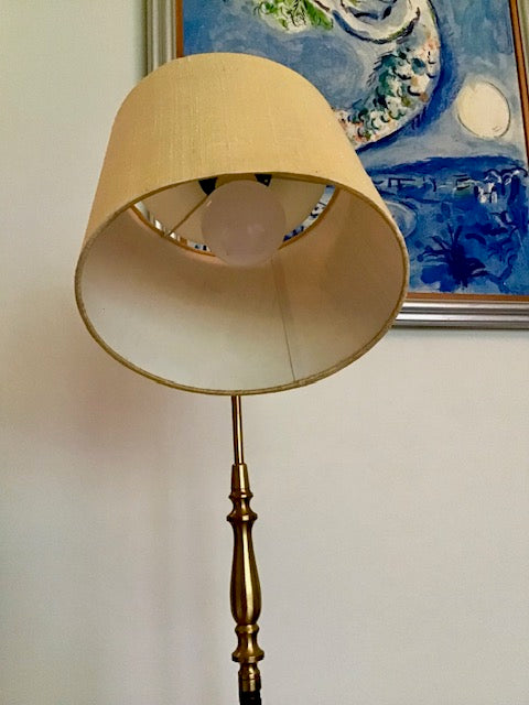 Floor lamp with beige shade and brass base against a wall with a painting.