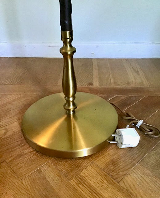 Brass lamp base on a wooden floor with a white wall in the background
