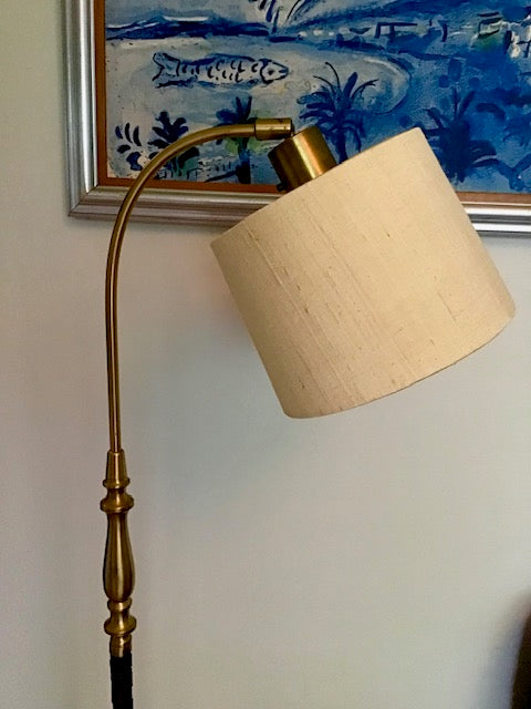 Wall-mounted lamp with beige shade and gold arm against a blue and white abstract painting.