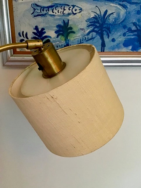 Beige lampshade with brass fitting against a blue palm tree painting