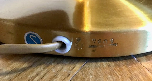 Close-up of a brass object with a brand logo and numbers on a wooden surface