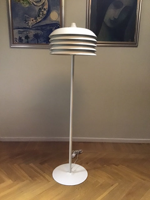 Modern floor lamp with white base and cylindrical shade in a room with a painting on the wall.