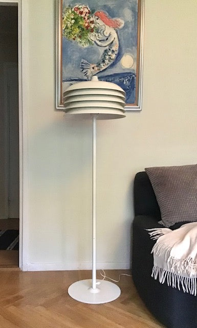 White floor lamp in a room with a painting on the wall and a couch.