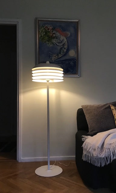 Floor lamp in a room with a painting on the wall and a couch.