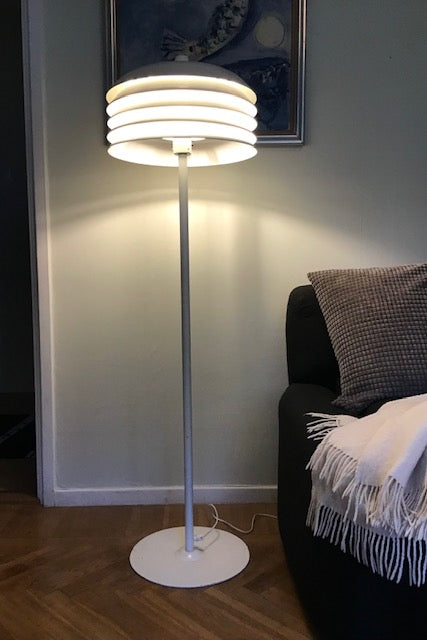 Modern floor lamp with a white base and cylindrical shade in a living room setting.