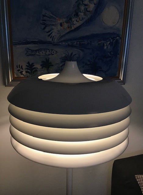 Modern lamp with a black base and white shade in front of a painting