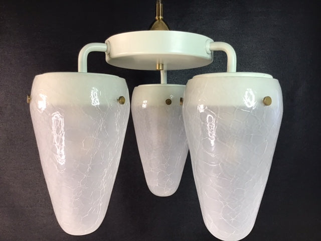 Vintage-style chandelier with three white glass shades on a dark background