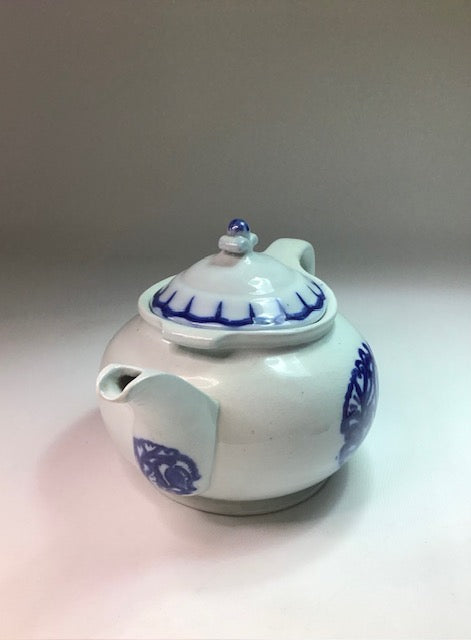 White ceramic teapot with blue floral patterns on a gradient background