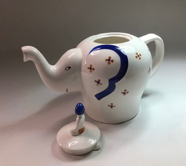 White ceramic teapot shaped like an elephant with a blue trunk on a gray background