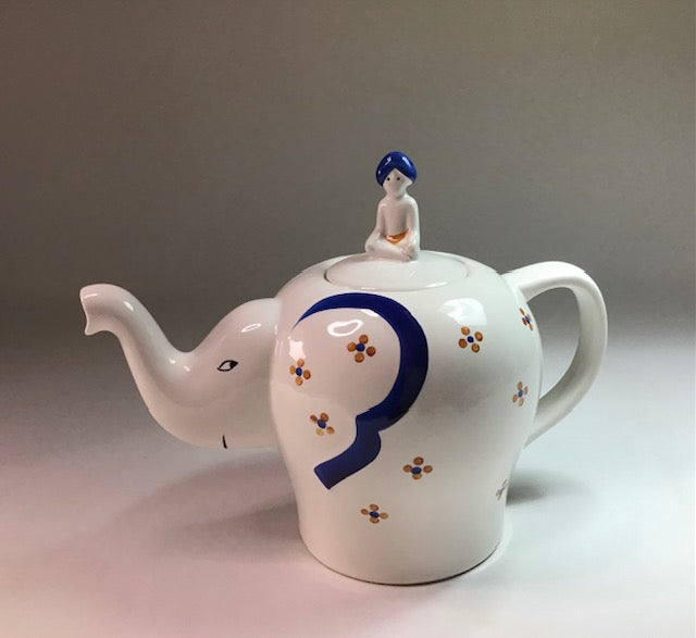 Ceramic teapot with elephant design and figure on top against a neutral background