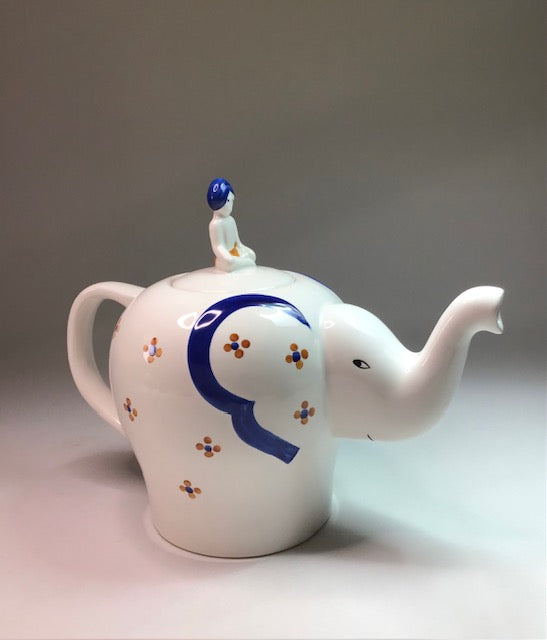 White ceramic teapot shaped like an elephant with a blue 'Q' and small figures on a gray background