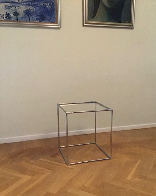 Glass side table on a wooden floor with framed artwork on the wall.