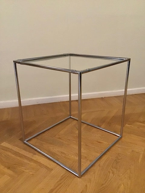 Metal frame with glass top on a wooden floor against a beige wall