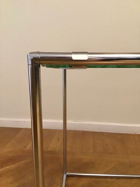 Glass table with metal frame on a wooden floor against a beige wall